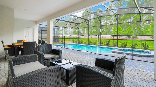 An outdoor patio area with wicker furniture, a pool, and a view of the surrounding greenery.