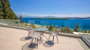 A balcony with a glass railing, two chairs, and a table overlooking a body of water and distant mountains. - Villa Ino Lefkas - Four Bedroom Villa, Sleeps 8 (Perigiali)