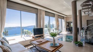 A modern living room with a large TV, a wooden coffee table, and a view of a lake. - Villa Ino Lefkas - Four Bedroom Villa, Sleeps 8 (Perigiali)