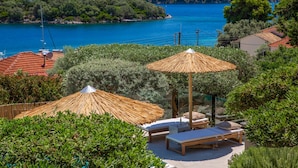 Une villa située sur la côte, dotée d’un espace extérieur aménagé, d’un toit de chaume et offrant une vue sur la mer et les collines.