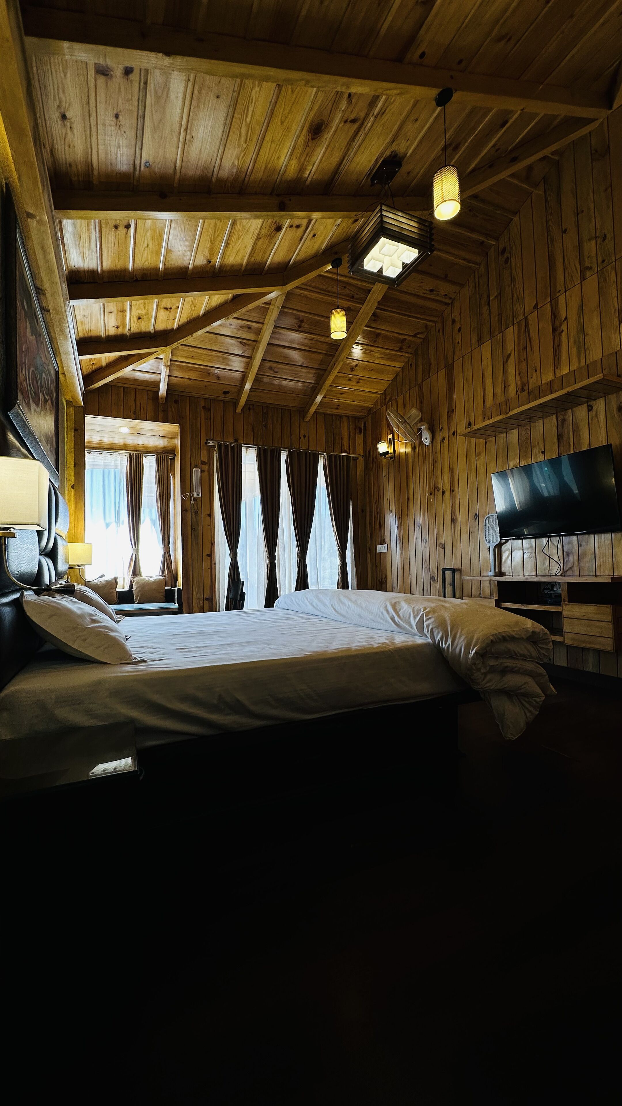 Une chambre dans un chalet en bois, avec un lit, une télévision et une fenêtre avec des rideaux.