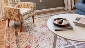 A room with a large window, a floral armchair, a patterned rug, and a round table with a book and a tray. - Myrtles on Madison House near ACU (Abilene)