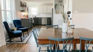 A modern kitchen with white cabinets and a dining area with a wooden table and blue chairs. - Myrtles on Madison House near ACU (Abilene)