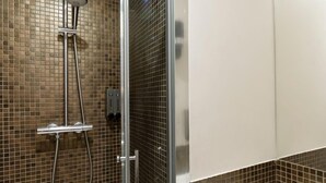 Une salle de bain moderne avec une douche à parois de verre, un lavabo blanc et des murs recouverts de mosaïques.