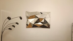 Un salon moderne avec un canapé brun foncé, une œuvre d’art géométrique accrochée au mur et un grand lampadaire.