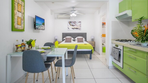 Una habitación moderna y compacta con cama, zona de comedor con sillas, pequeña cocina con estufa y ventilador de techo.