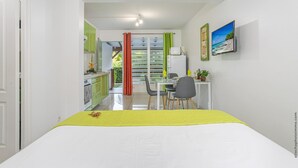 Un dormitorio con cama, escritorio y silla, una mesita con planta y ventana con cortinas.