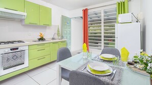 Una cocina moderna con gabinetes verdes, una estufa a gas y un área de comedor con una mesa de vidrio preparada para dos personas.