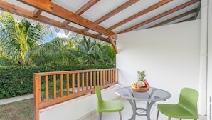 Un patio techado con baranda de madera, una mesa de vidrio y dos sillas verdes.