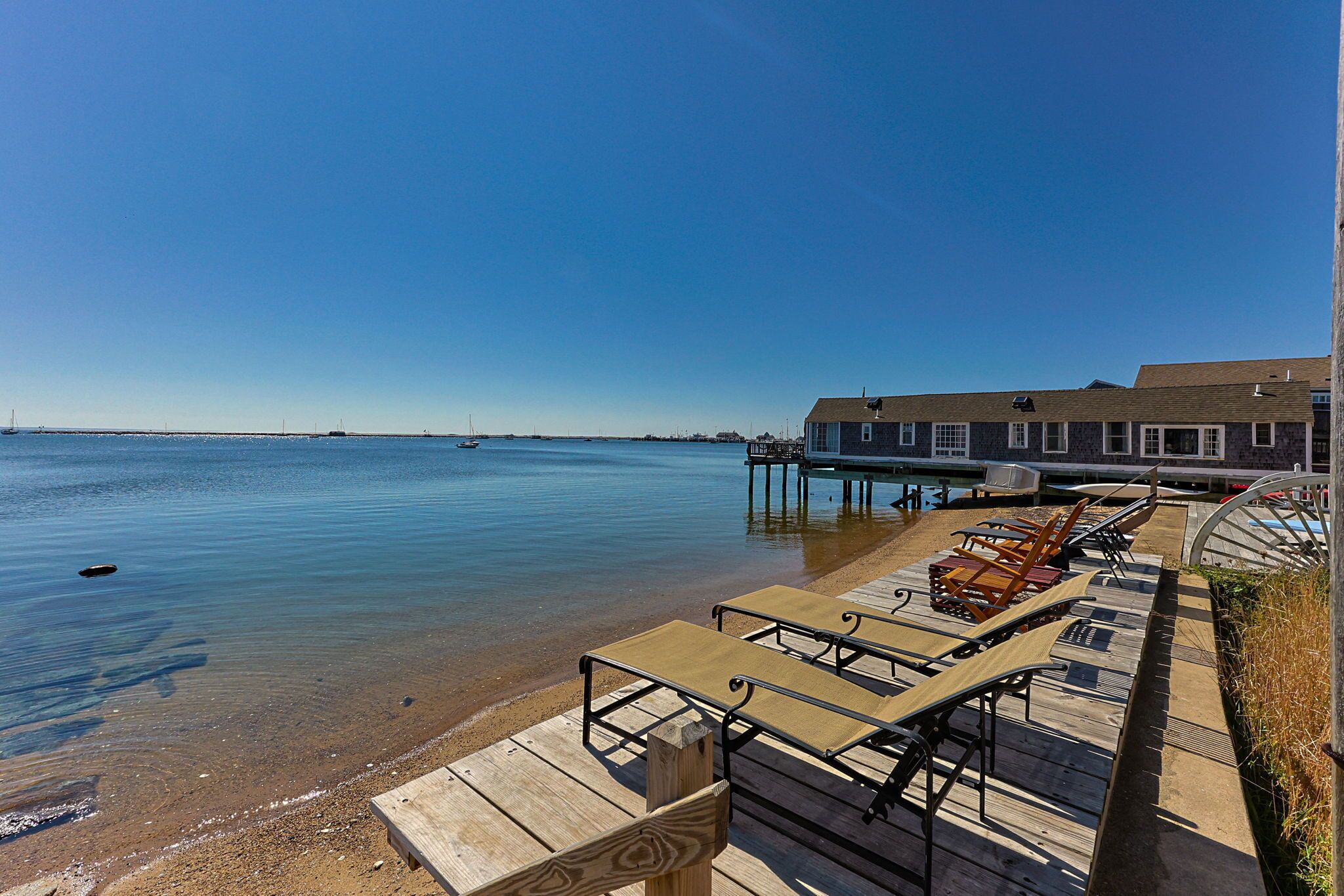 Une terrasse en bois avec des chaises longues et un espace aménagé au bord de la piscine, offrant une vue sur une étendue d’eau calme, avec une jetée qui s’avance sur l’eau.