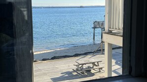 Une terrasse en bois avec des tables de pique-nique, donnant sur une mer calme, et une jetée avec un poste de surveillance pour les sauveteurs.