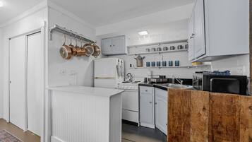 Una cocina compacta con armarios blancos, estufa, microondas y pileta.