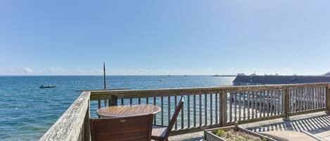 A wooden deck with a table and chairs overlooking a calm sea with boats.