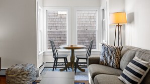 Un salon avec une table ronde et deux chaises, un canapé agrémenté de coussins à motifs et un lampadaire.