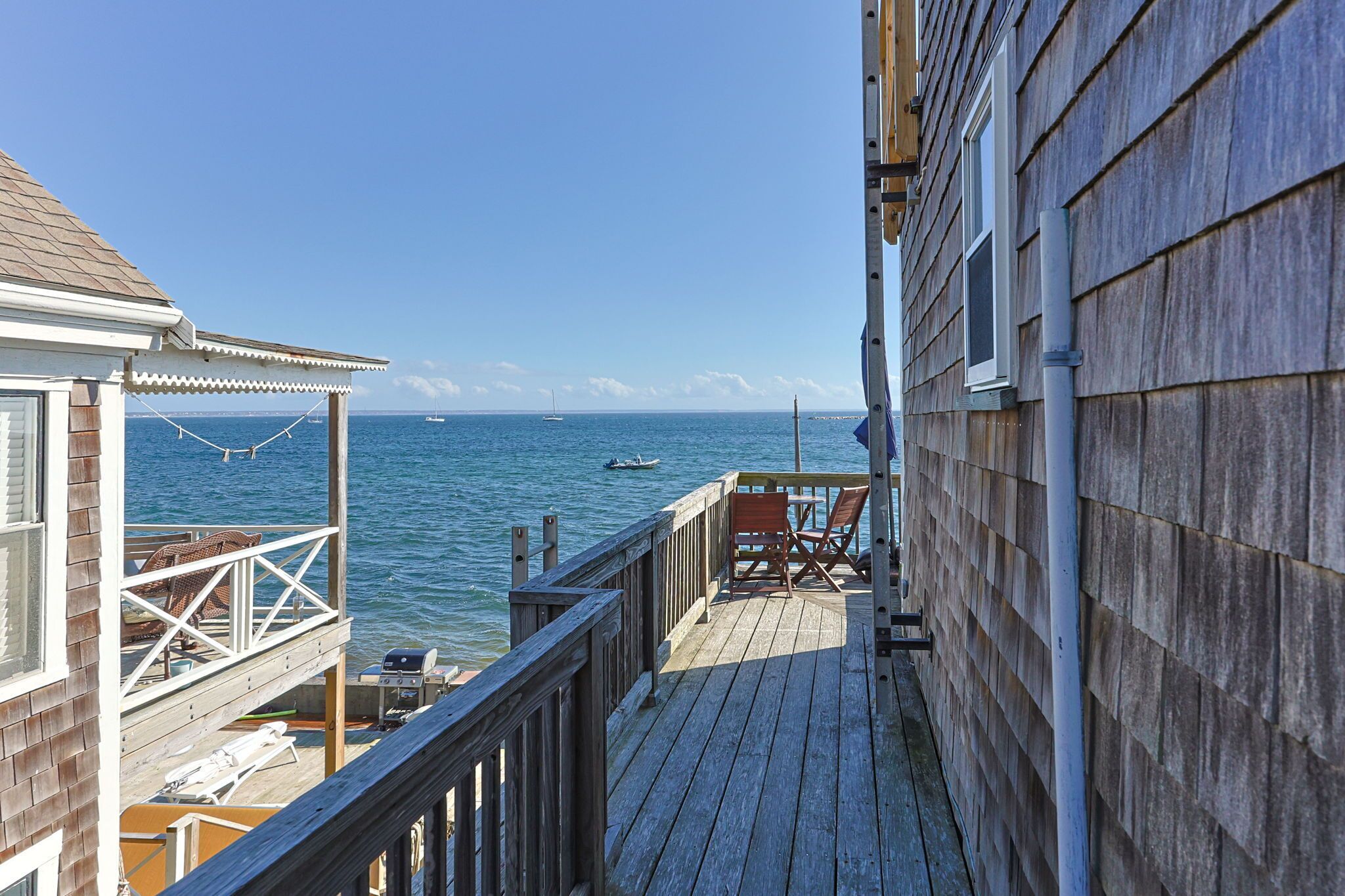 Une terrasse en bois offrant une vue sur la mer, un bateau et un voilier au loin.