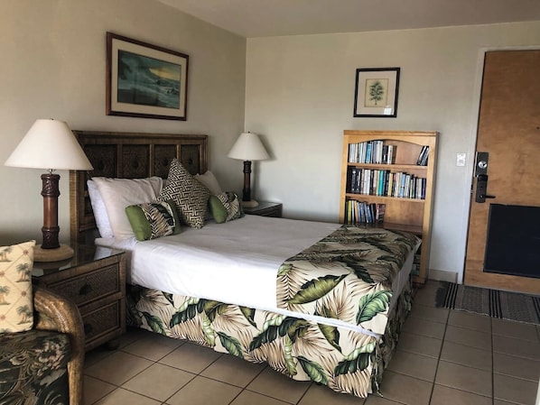 A bedroom with a bed, two bedside tables with lamps, a bookshelf, and a door.