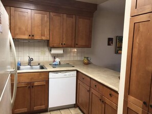 A kitchen with wooden cabinets, a white dishwasher, a sink, and a countertop. - One Bedroom Ocean View (Kihei)