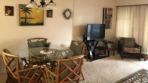 Ein Wohnzimmer mit rundem Glastisch, Korbstühlen, einem Fernseher und einem Deckenventilator.