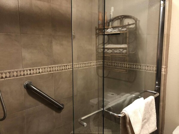 Une douche avec une porte en verre, un porte-serviettes et un étagère pour les produits de douche.