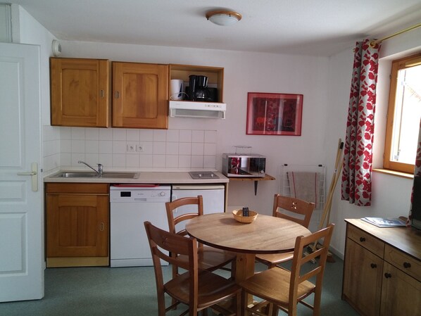 Een kleine keuken met houten kastjes, een magnetron, een koffiezetapparaat en een eettafel met stoelen.