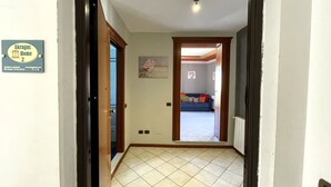 Un pasillo con suelo de baldosas, una puerta que da a una sala de estar con sofá y un cuadro en la pared.