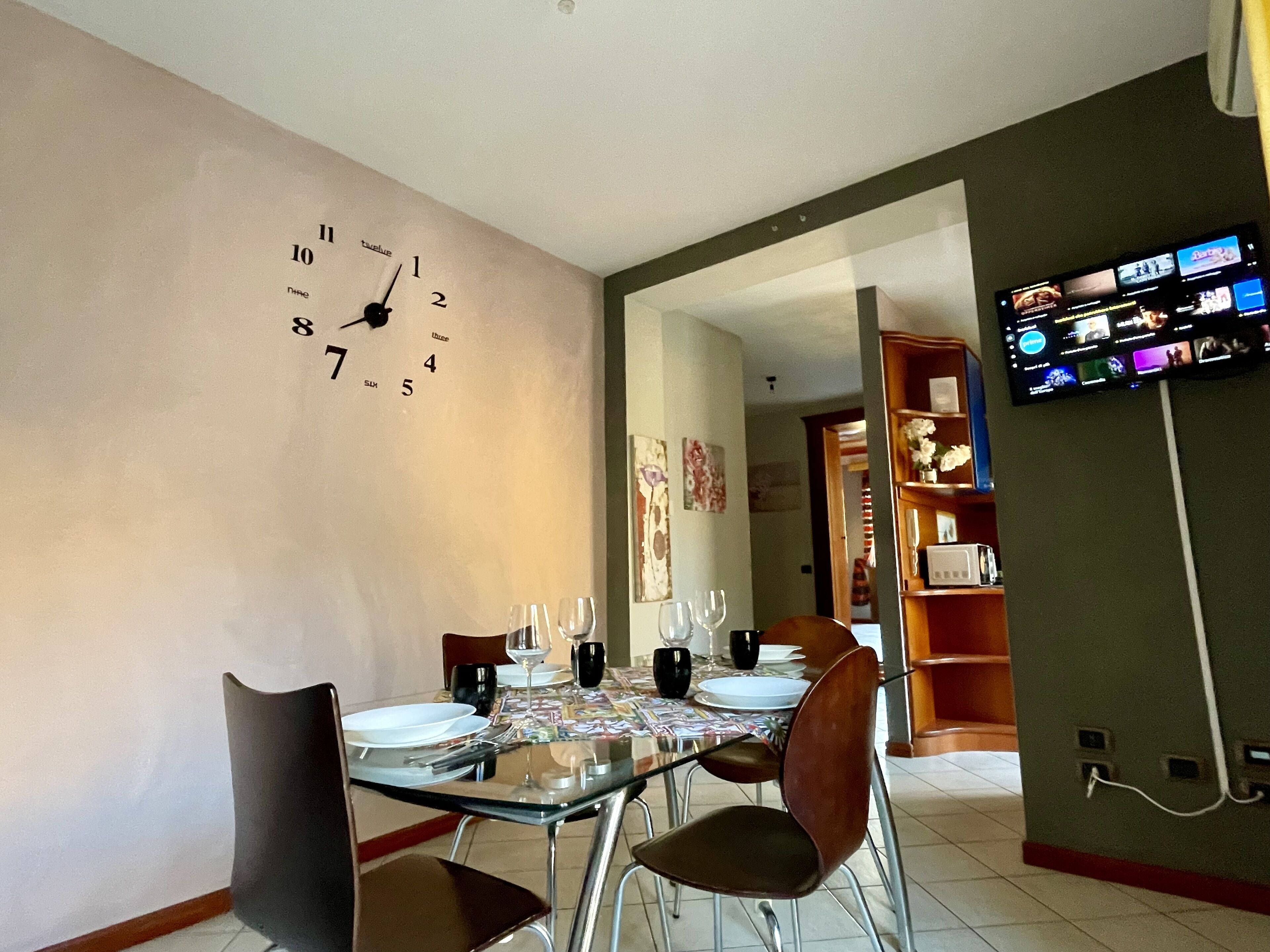 Ein Essbereich mit einem Tisch für vier Personen, einer Wanduhr und einem an der Wand befestigten Flachbildfernseher.