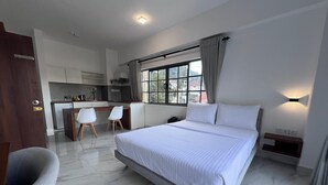 Une chambre d’hôtel moderne dotée d’un grand lit, d’un bureau avec des chaises, d’une kitchenette et offrant une vue sur l’extérieur.