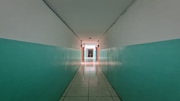 Un pasillo con paredes azul verdoso y piso de baldosas, que conduce a una puerta al final.