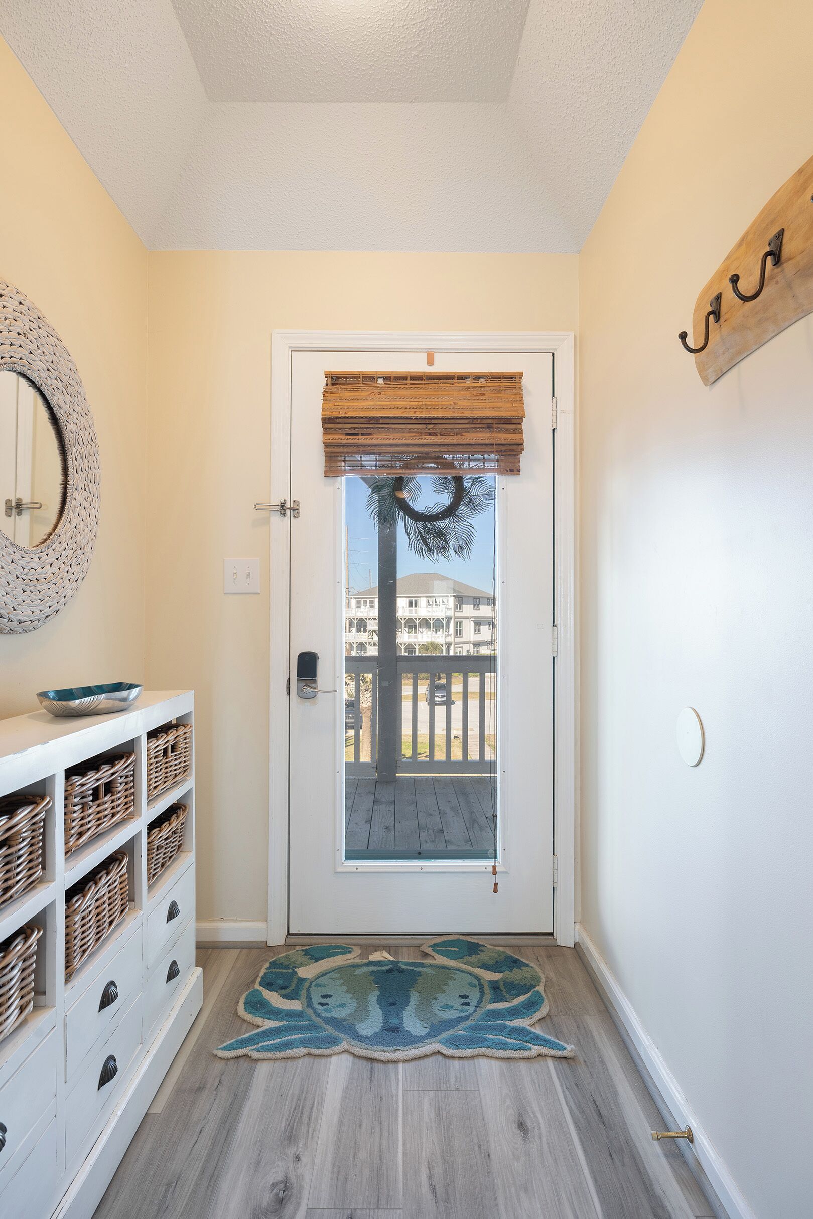 A hallway with a white door, wicker baskets on shelves, a blue rug, and a wooden sign on the wall.