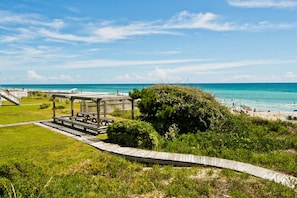 A beachside park with a wooden gazebo, picnic tables, and a boardwalk leading to the beach.