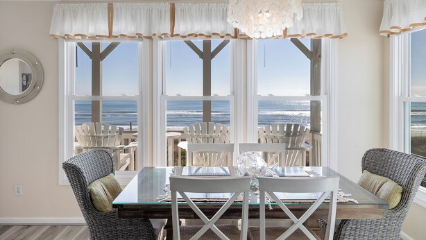 A dining area with a table and chairs, large windows with ocean views, and a chandelier. - Pier Pointe 3B2, Oceanfront Condo, in Emerald Isle, NC! (Emerald Isle)