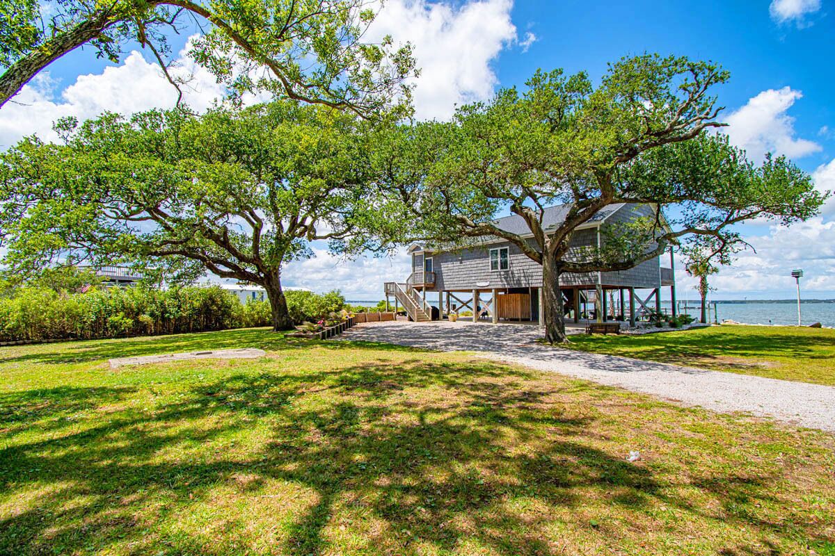 A house with a porch, a large tree in front, and a view of the water.