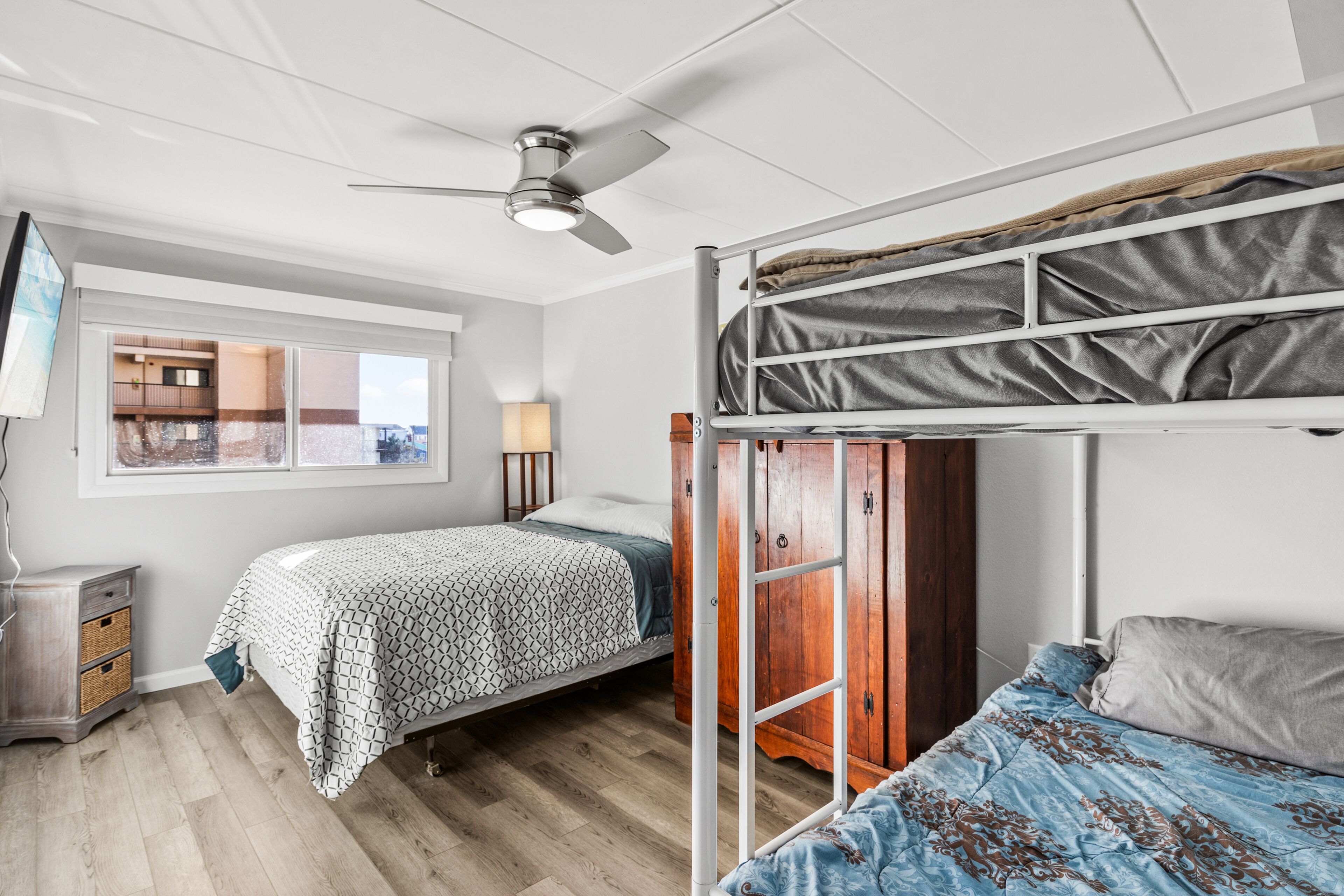 A room with two beds, a ceiling fan, a window, and a wooden wardrobe.