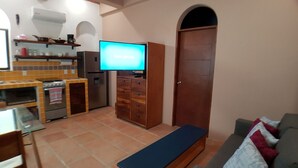 Un espacio habitable pequeño con kitchenette, televisión, sofá y banca.