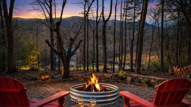 Un foyer avec deux fauteuils Adirondack rouges, une petite table avec des collations et des boissons, le tout entouré d’un mur de pierres et avec une forêt en arrière-plan.