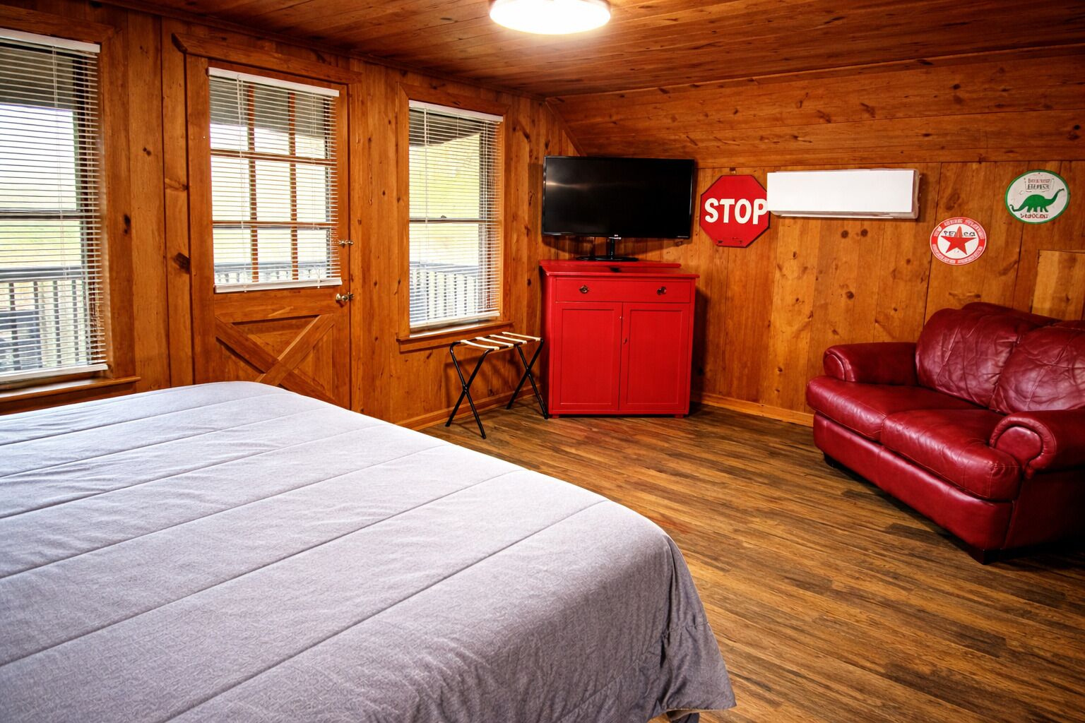A room with a bed, a red leather couch, a television, a red cabinet, and a stop sign on the wall.