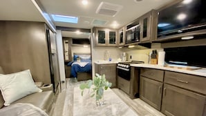 A compact kitchen with a stove, microwave, and cabinets. A small plant is on the floor. - Relax to the Sound of the River while you soak in a Private Hot Tub  (Carmel Valley)