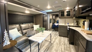 A compact RV interior with a kitchenette, a seating area with a table, and a bed. - Relax to the Sound of the River while you soak in a Private Hot Tub  (Carmel Valley)
