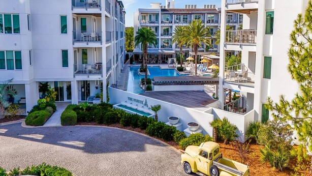 A modern hotel with a swimming pool, multiple balconies, and a vintage car parked in front. - The Pointe by Southern Vacation Rentals (Panama City Beach)