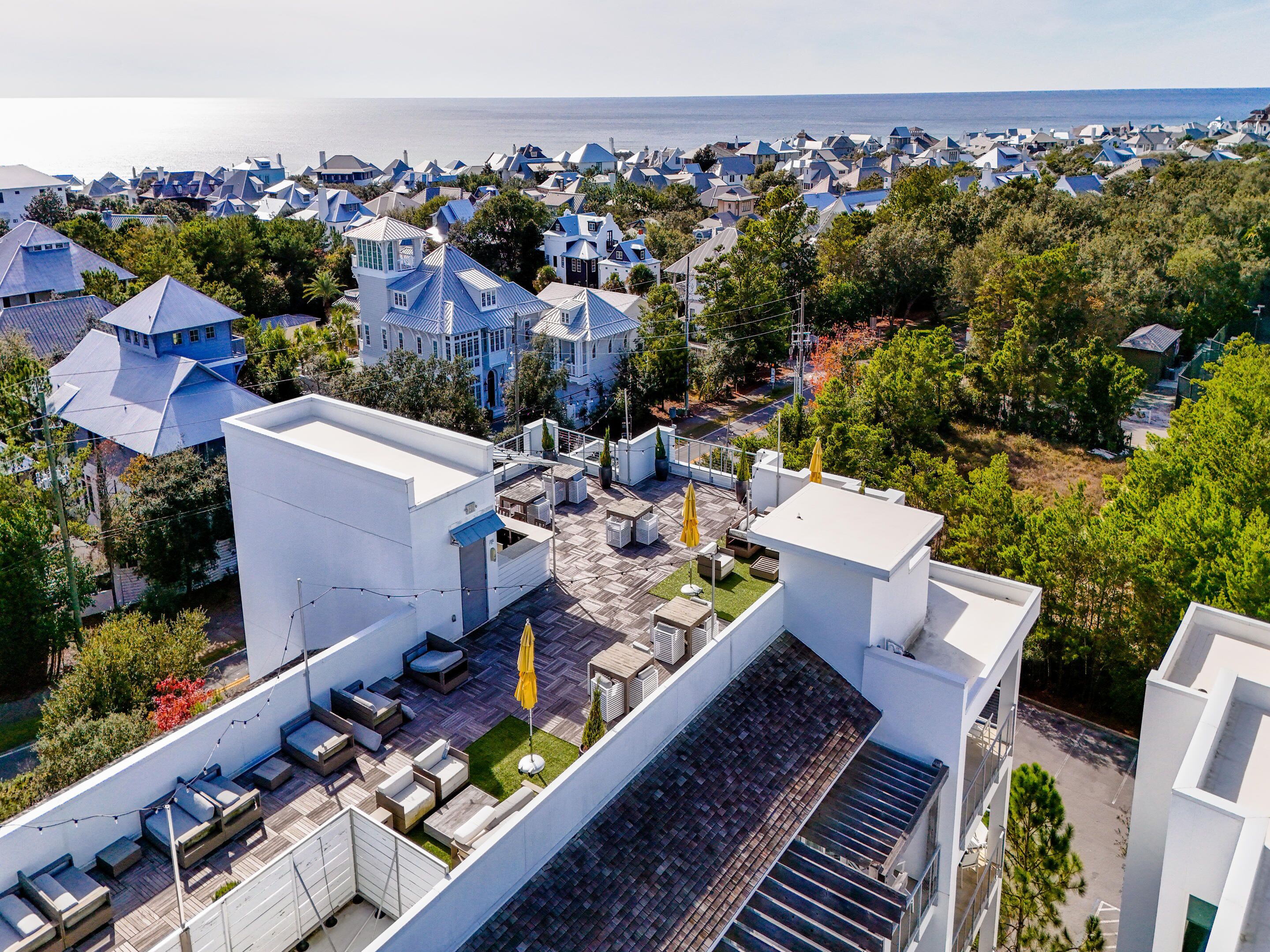 A residential area with modern houses, a rooftop patio with outdoor furniture, and a view of the sea.