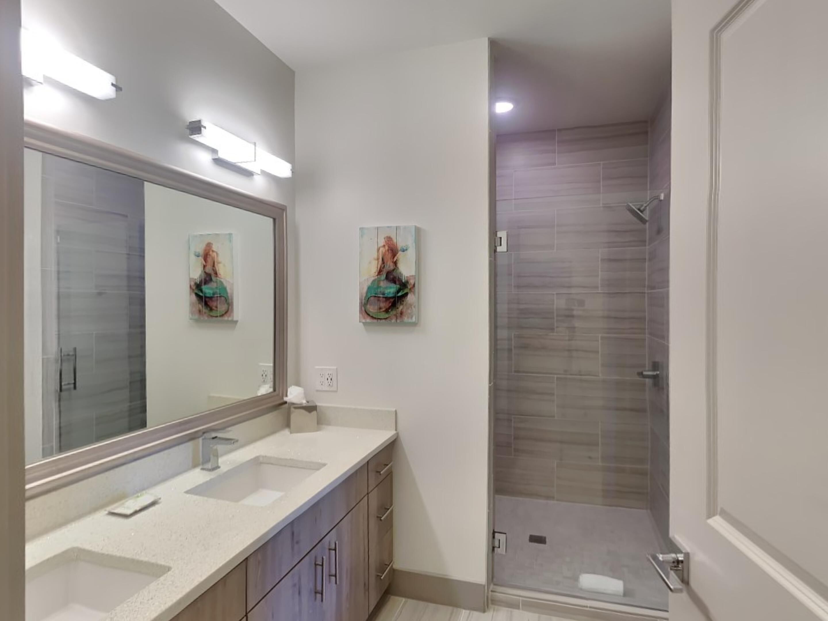 A modern bathroom with a large mirror, two sinks, and a walk-in shower.