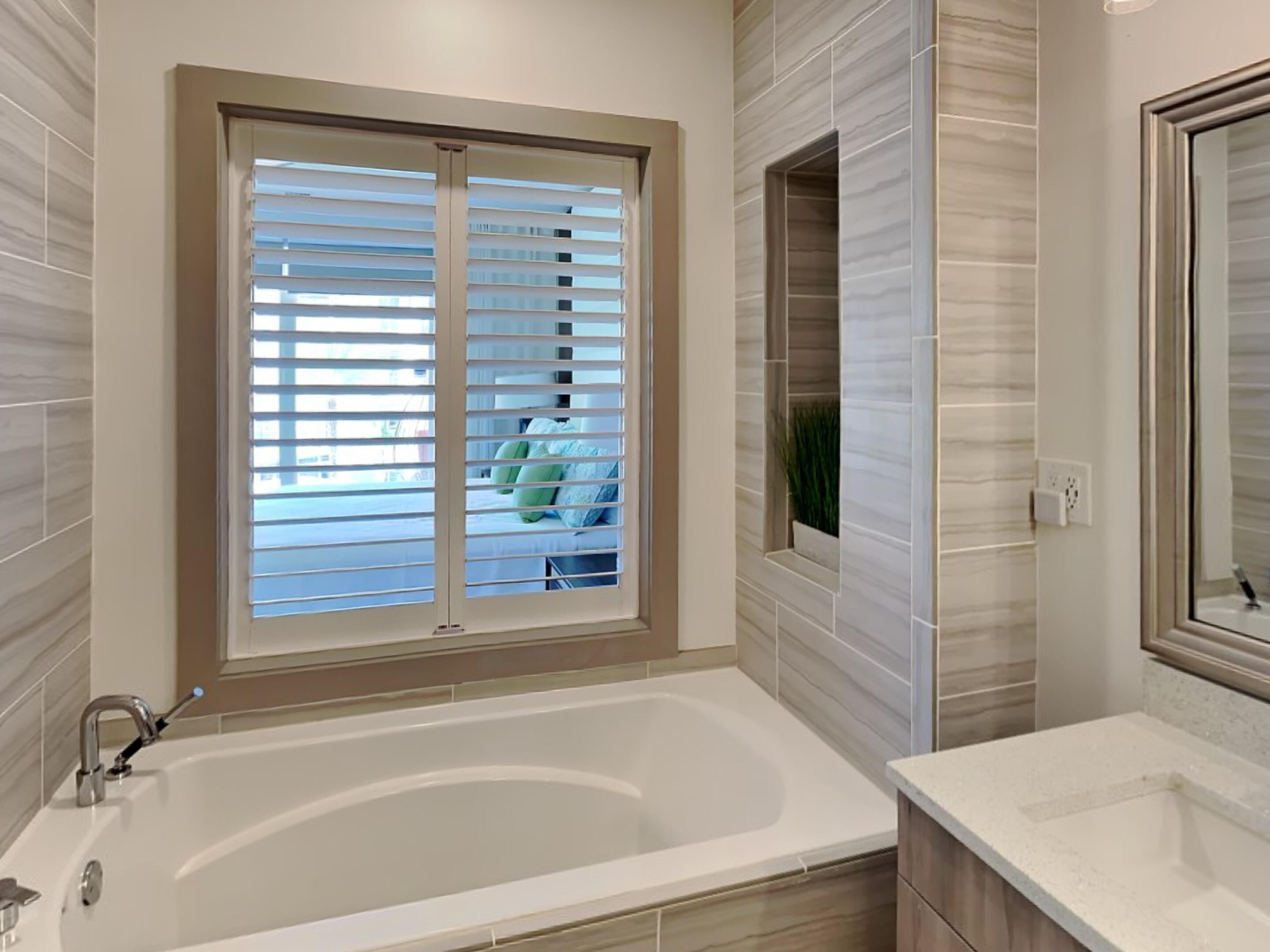 Un baño con bañera, una ventana con persianas y un espejo.
