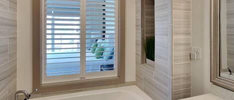 Un baño con bañera, una ventana con persianas y un espejo.