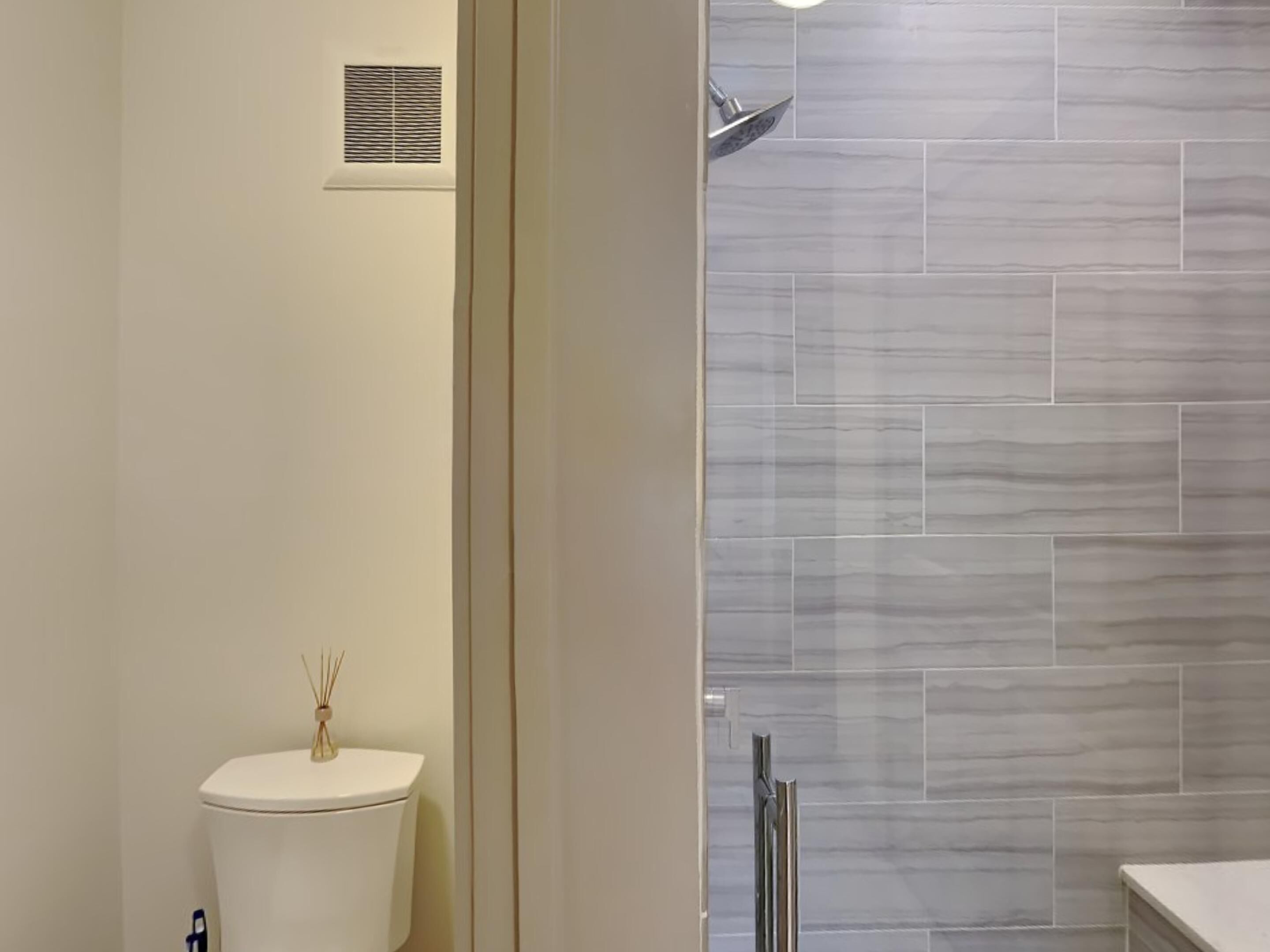 A bathroom with a toilet, a shower with a rain showerhead, and a tiled wall.