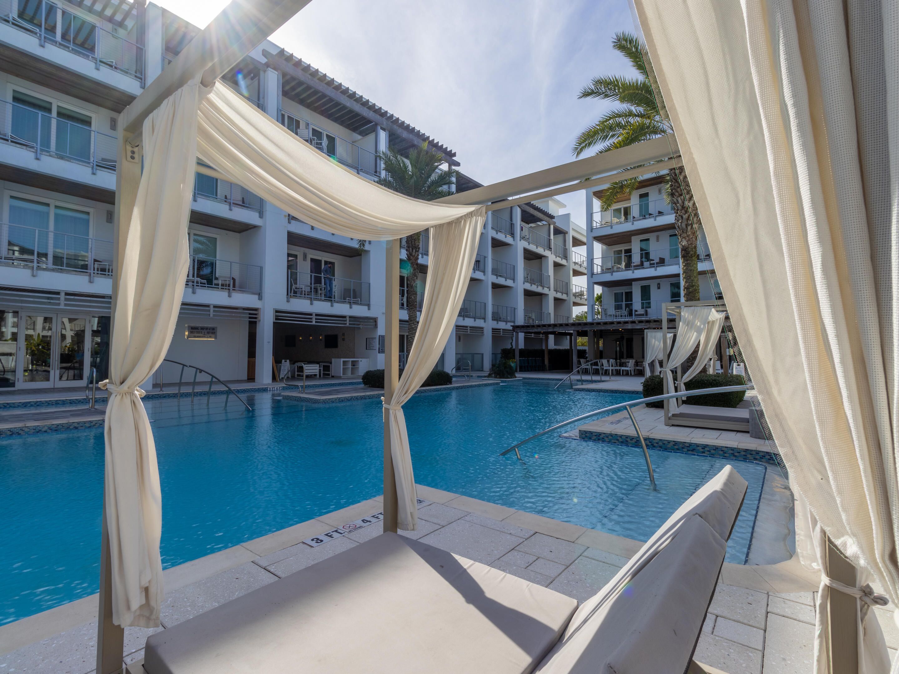 Zona de piscina con vista despejada, sillas de descanso y un edificio de varios pisos con balcones.