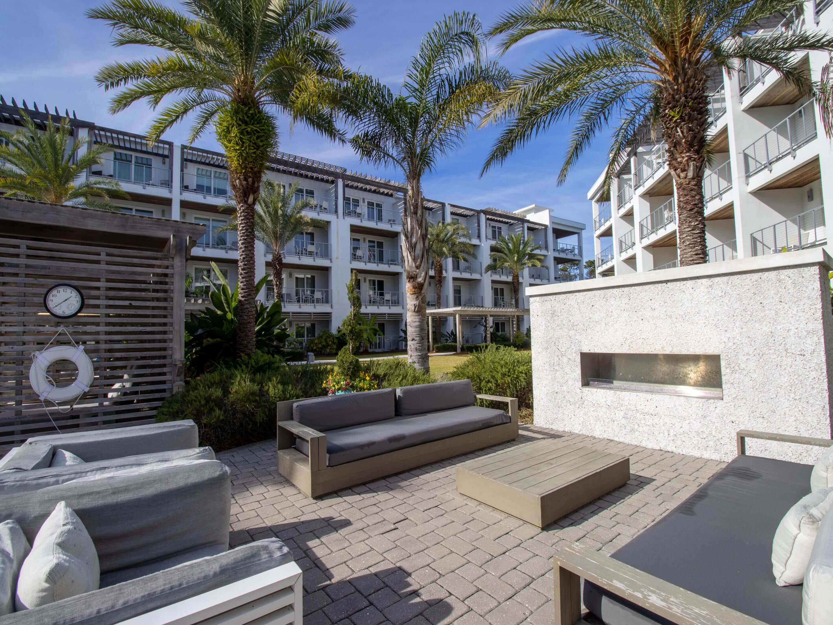 An outdoor patio area with a sofa, a small table, and a clock on a wooden fence.