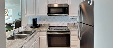 A modern kitchen with white cabinets, stainless steel appliances, a built-in oven, and a coffee maker.