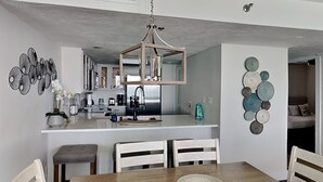 Une cuisine moderne avec des meubles blancs, un îlot central et un coin repas comprenant une table en bois et des chaises blanches.