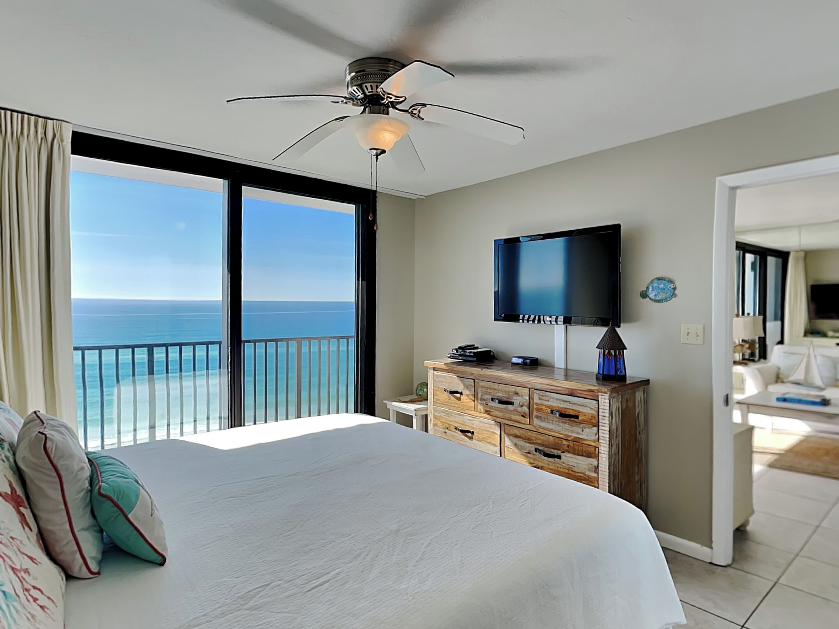 A hotel room with a large bed, a ceiling fan, a TV, and a view of the ocean.