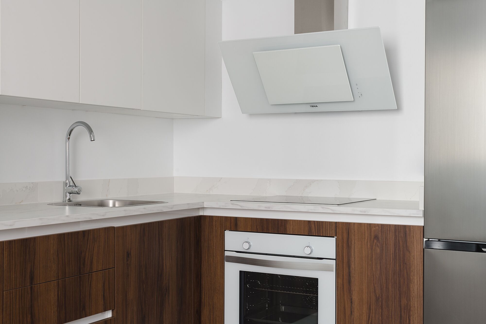 Une cuisine moderne dotée d’un évier en acier inoxydable, d’un four encastré et de meubles de rangement en bois.